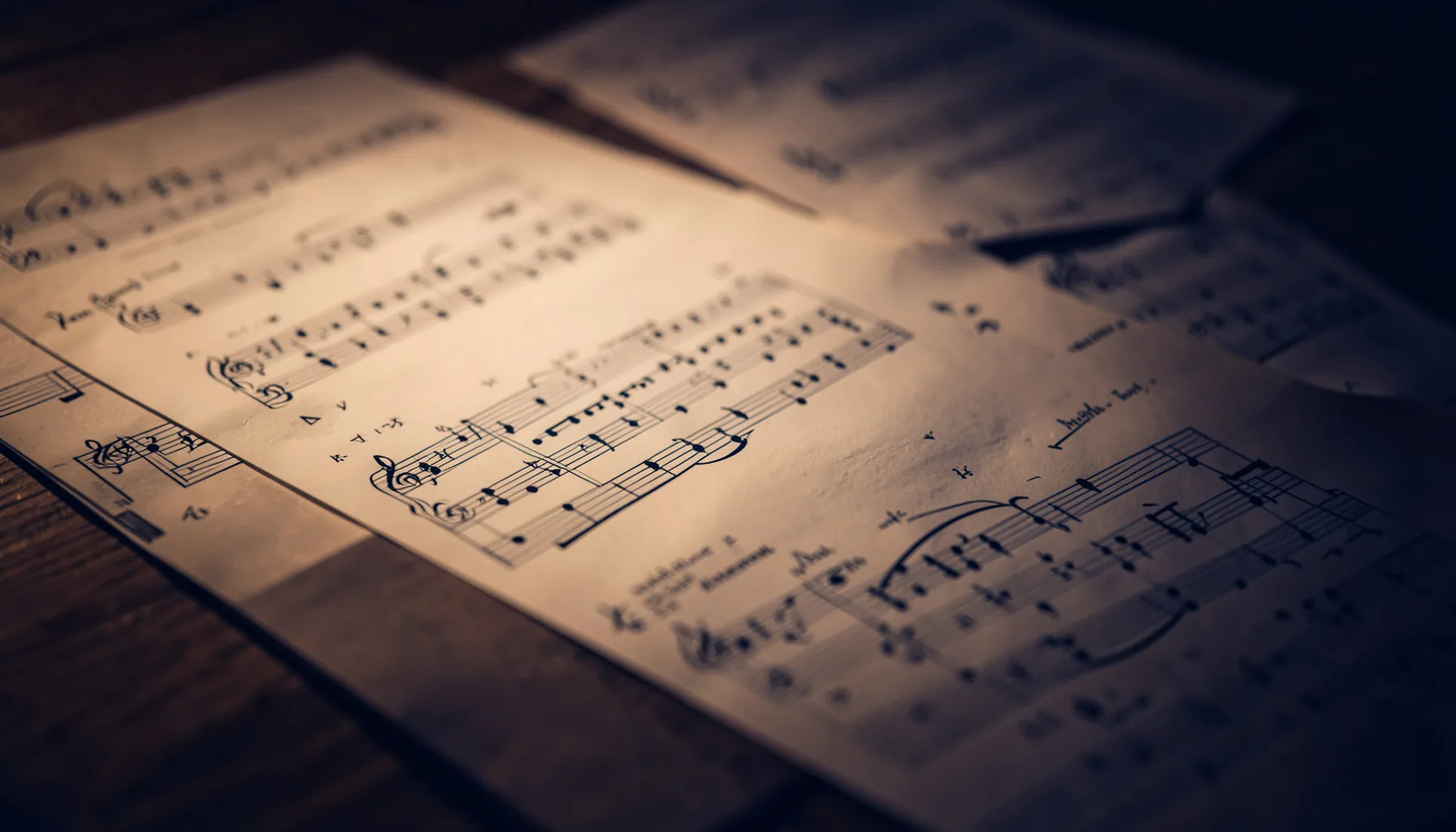 Softly lit sheet music pages on a dark wooden surface, warm amber and deep navy tones