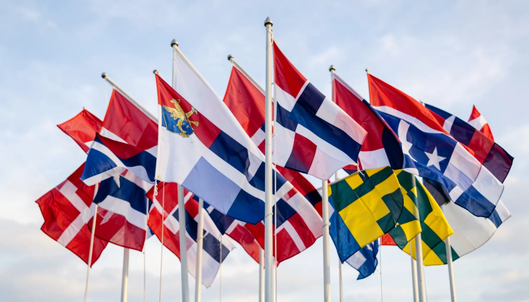 A cluster of Nordic flags against a soft sky, red white blue and yellow cross designs