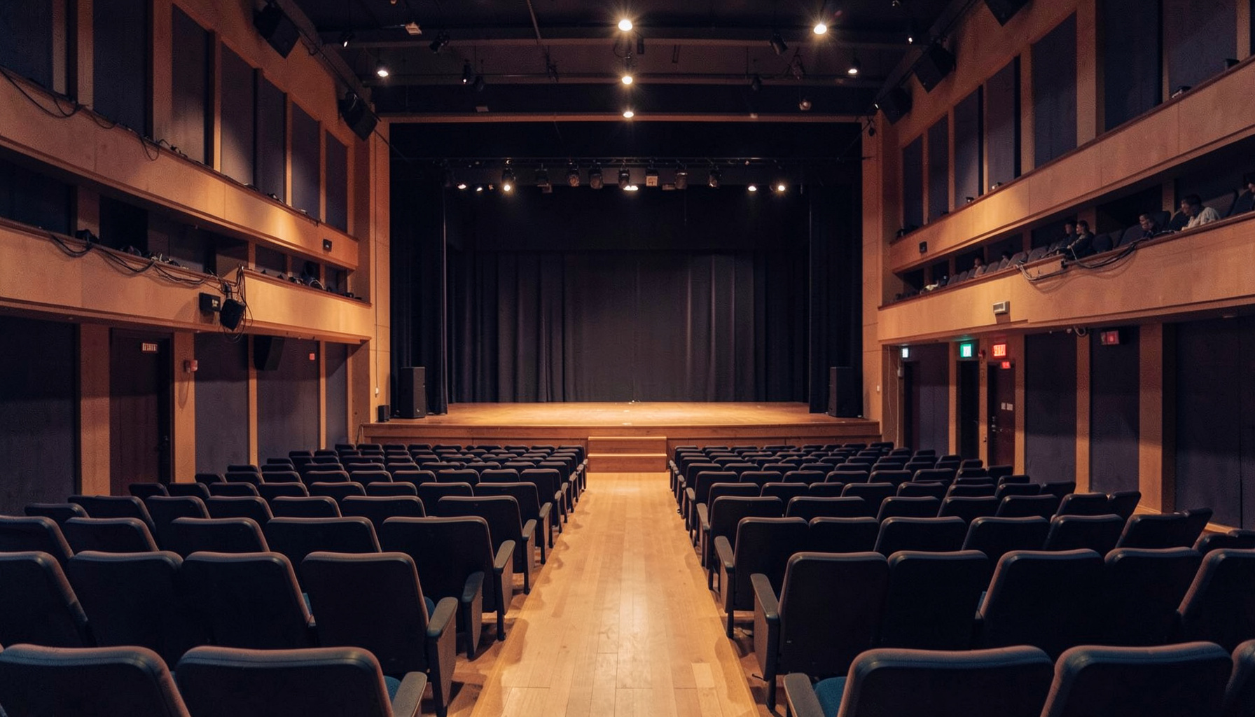 A softly lit concert hall interior with warm amber and navy tones, rows of empty seats facing a stage